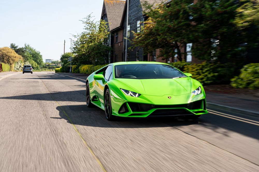Lime green Lamborghini Huracan Evo driving on a residential road surrounded by trees and houses.
