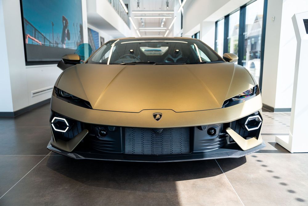 Matte gold Lamborghini Huracan EVO displayed front-facing in a luxury car dealership showroom interior.