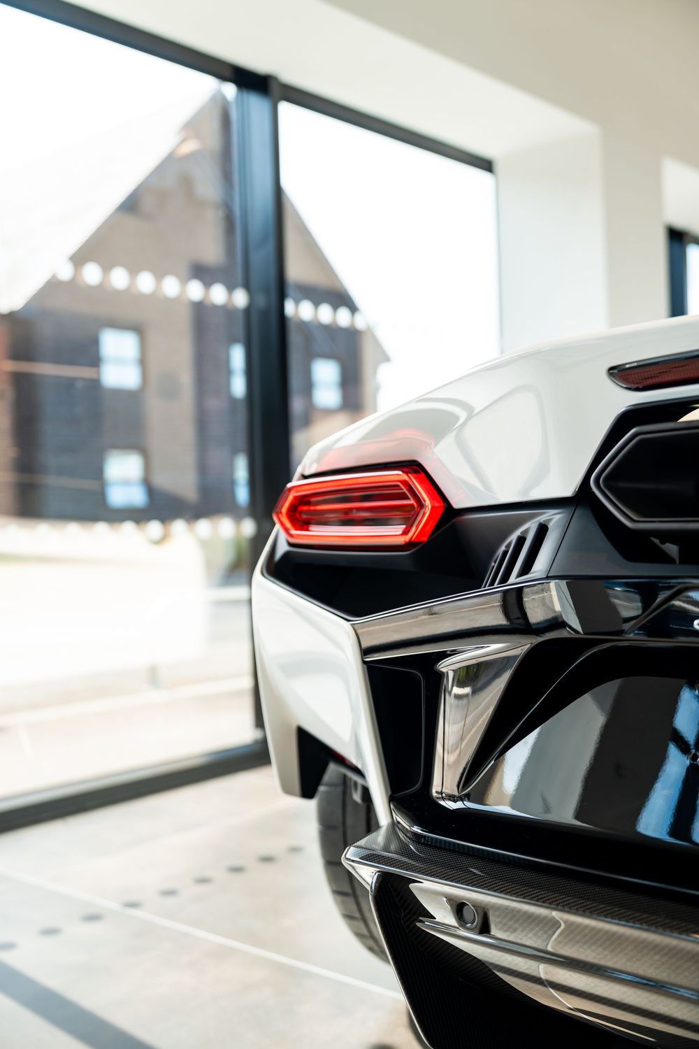 Rear view of a white Lamborghini supercar with distinctive red tail lights displayed in a modern showroom.