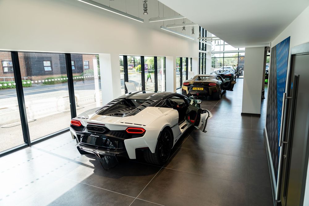 Multiple Lamborghini supercars including a white model displayed inside a bright, modern dealership showroom.
