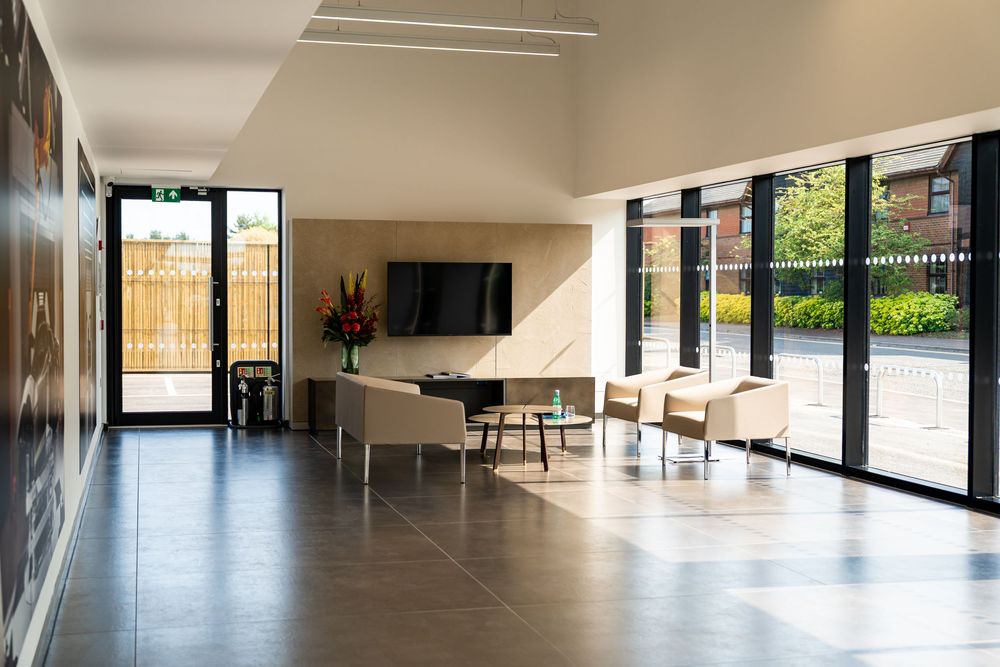 Modern car dealership reception lounge with large windows, natural light, and contemporary seating area.