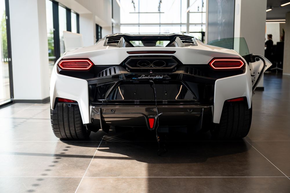 Rear view of a white Lamborghini supercar with red accents displayed in a luxury car dealership showroom.