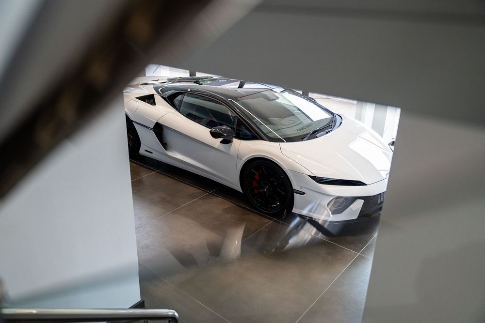 White Lamborghini supercar with black accents photographed from above in a modern showroom.