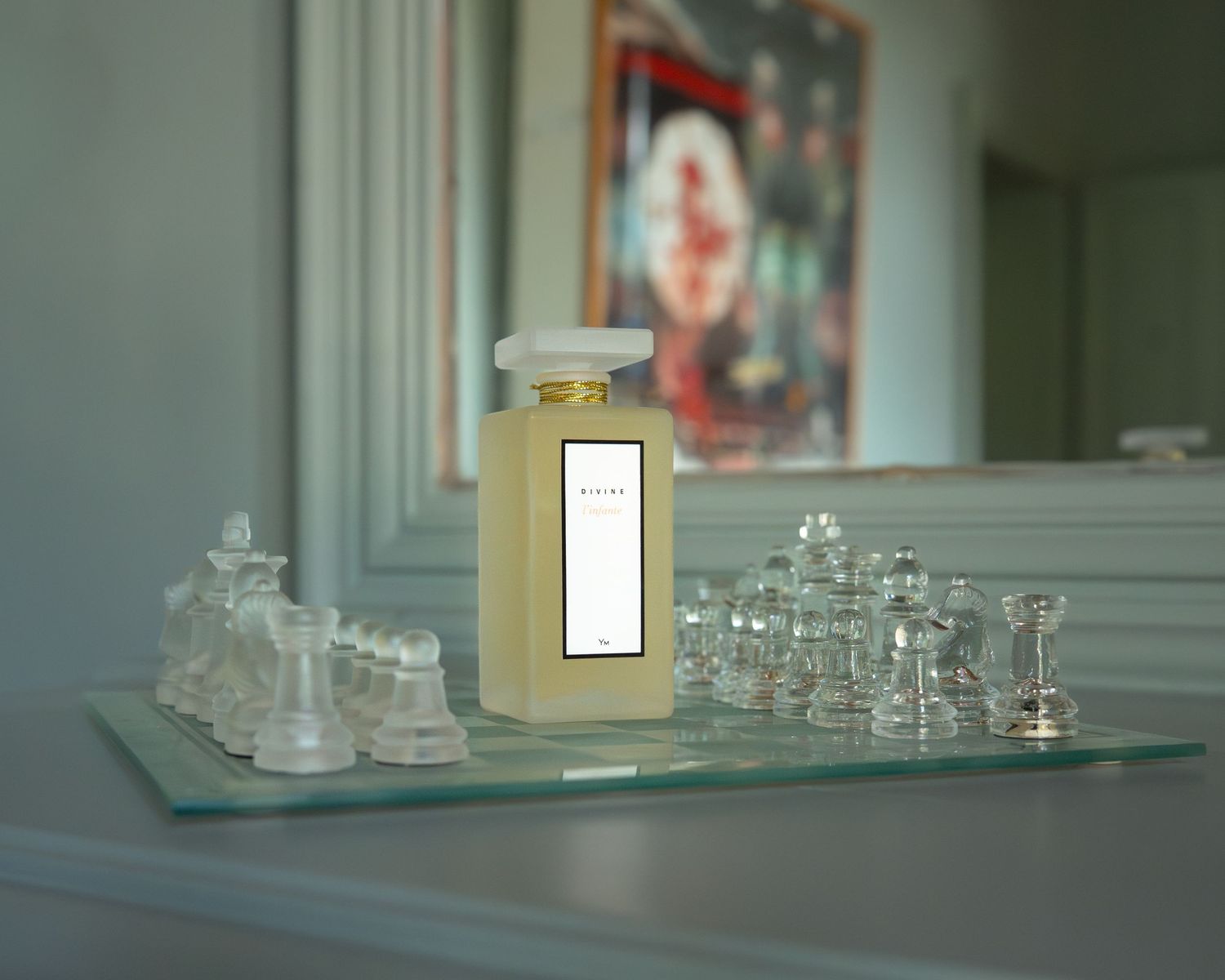 Un grand flacon de parfum Divine, posé sur un plateau en verre à côté d'un miroir, entouré de pièces d'échecs en cristal.
