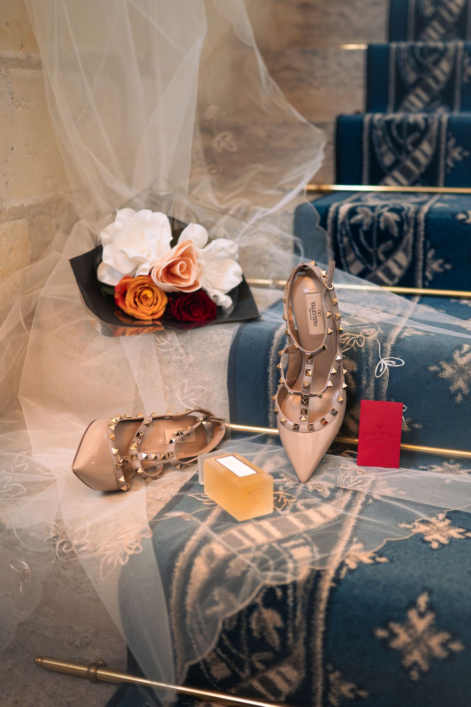 Valentino Rockstud nude heels displayed with roses and a veil on blue upholstered steps.