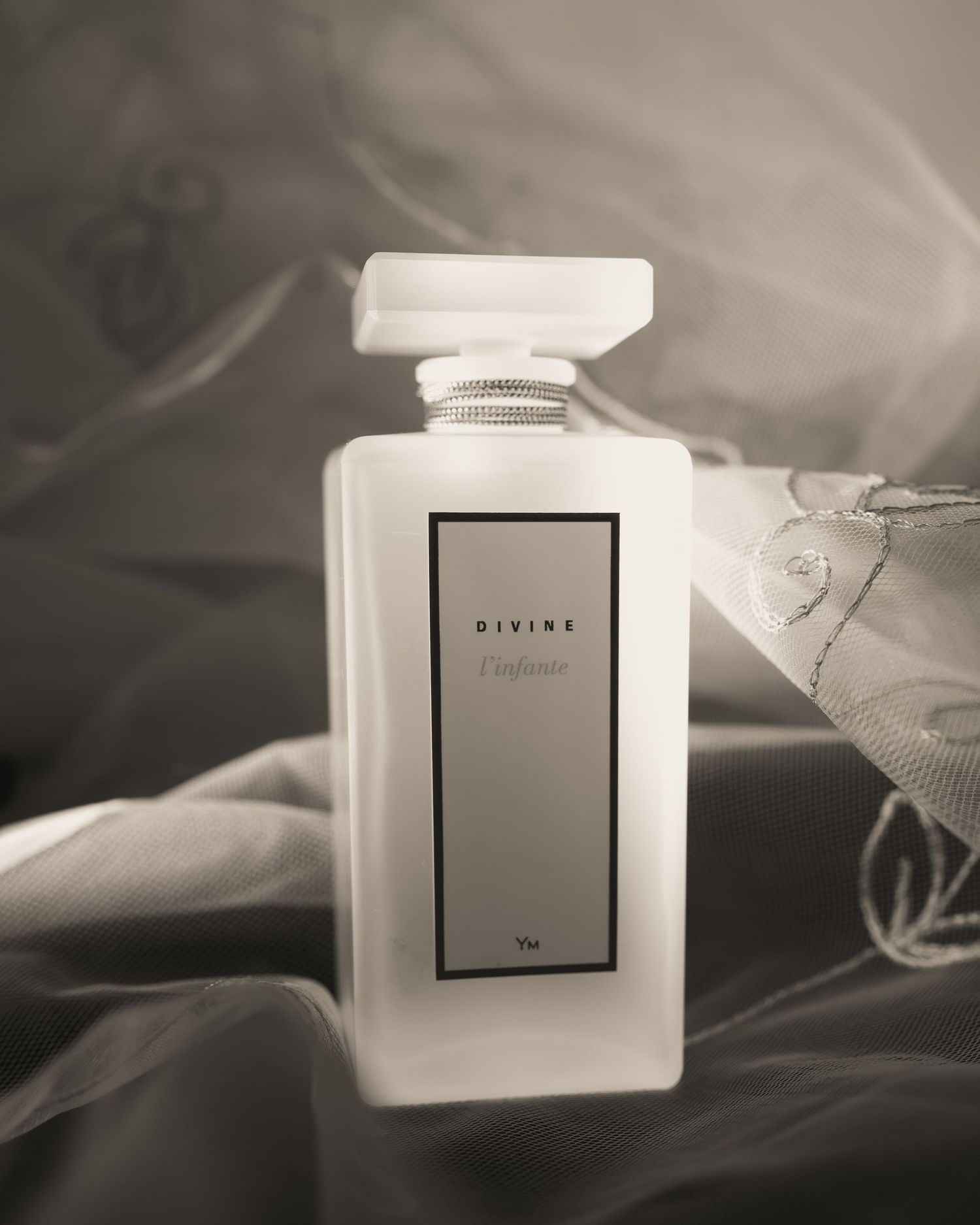 Élégant flacon de parfum carré blanc, sur un fond de voile de mariée. Photographe Stéphanie Lecaudé