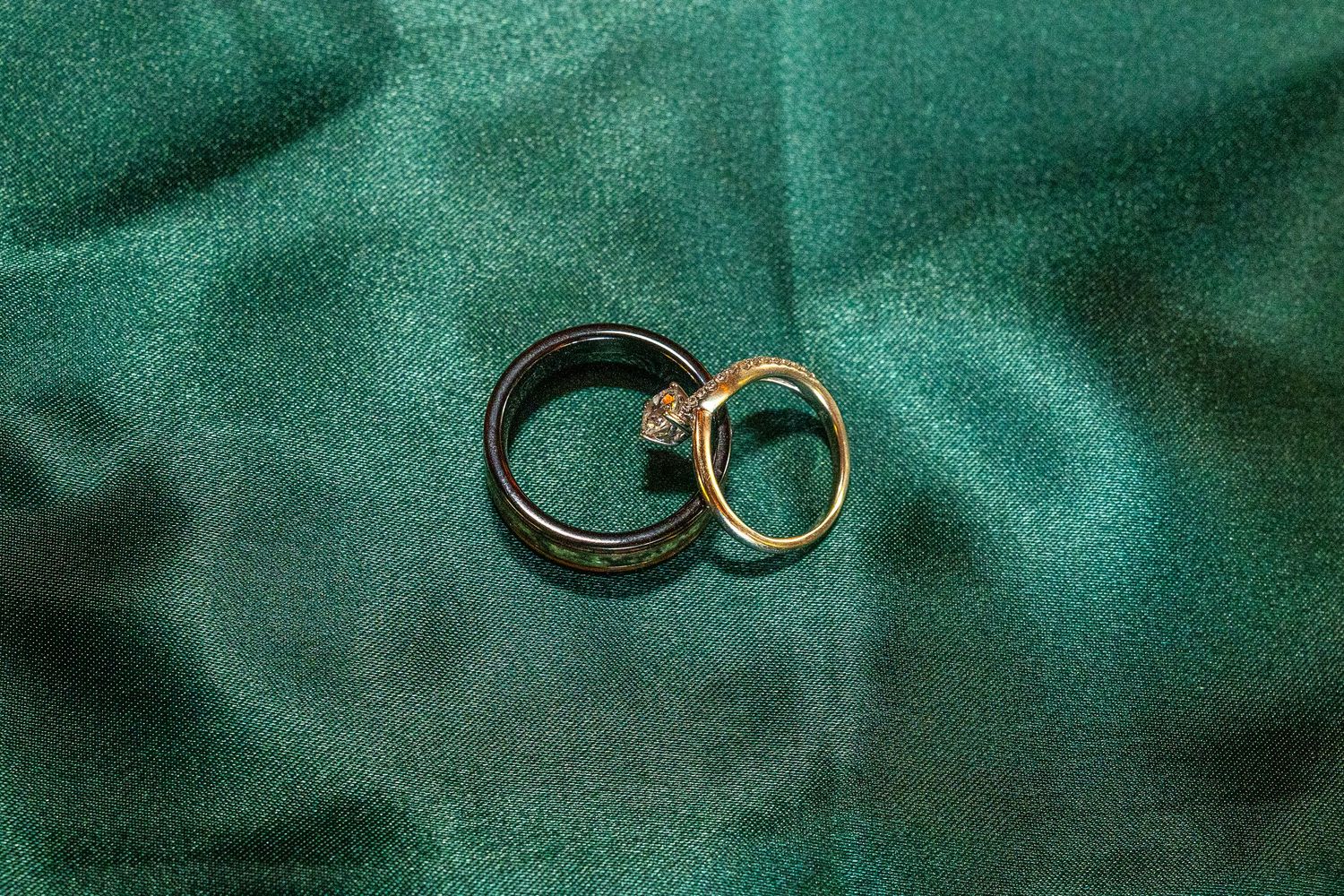 Two gold wedding rings intertwined on a green satin fabric background, symbolizing love and commitment.