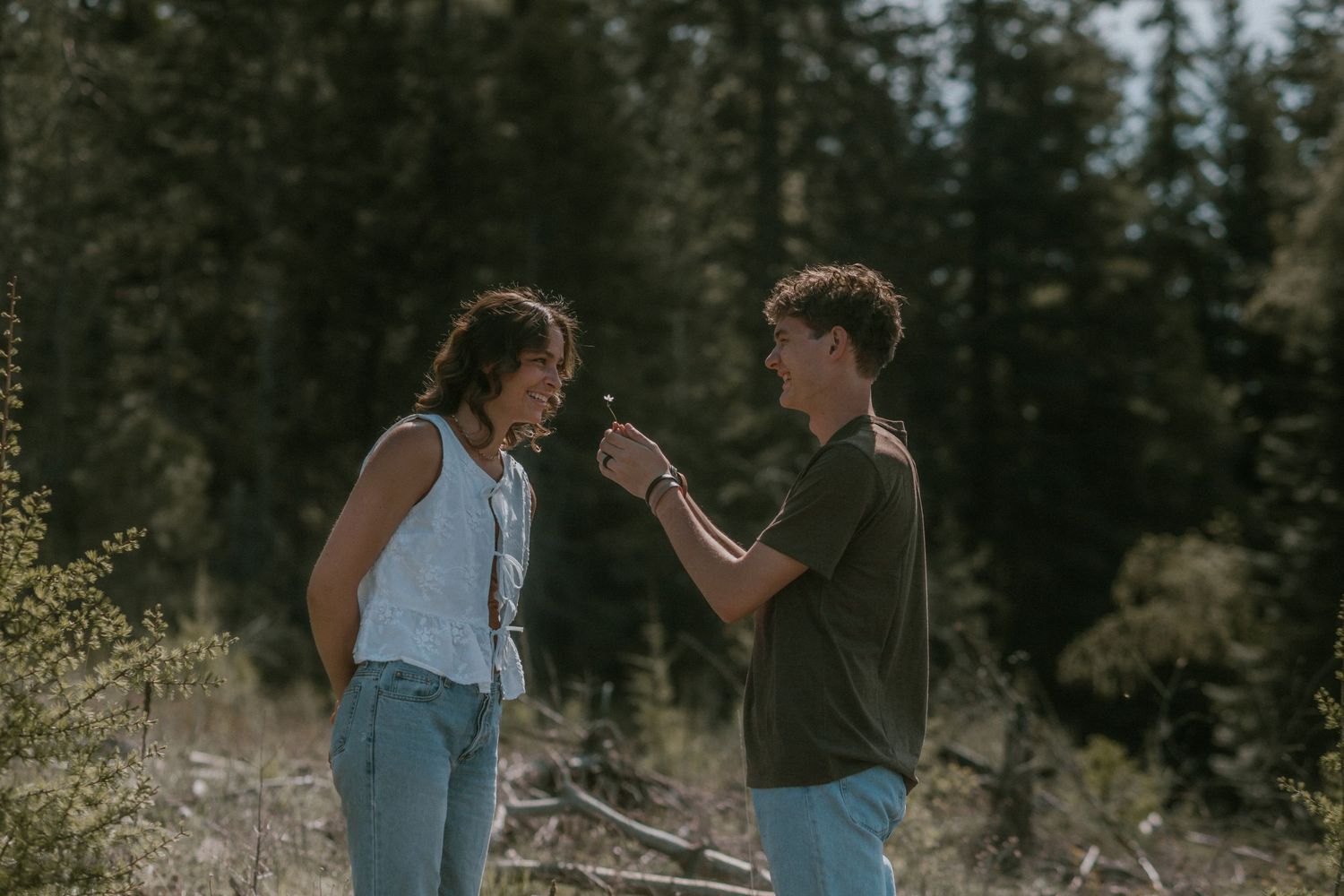 Young couple sharing a tender moment in a sunlit forest during an outdoor engagement session.
