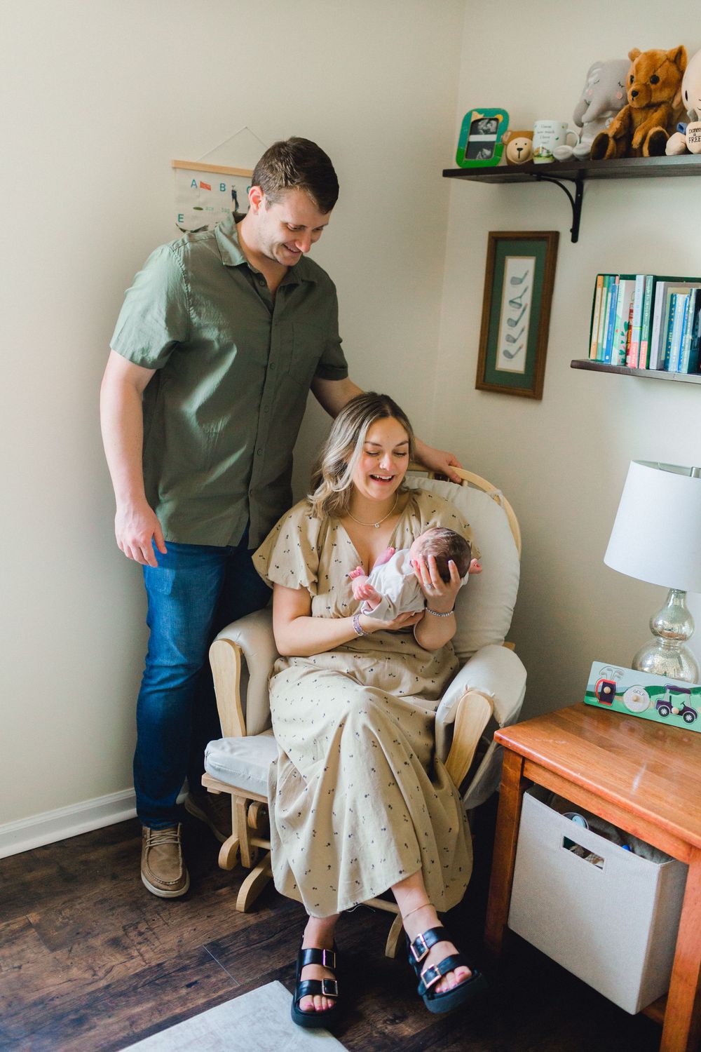 New parents admire their newborn baby in a cozy nursery, mother seated in a rattan chair holding the infant.