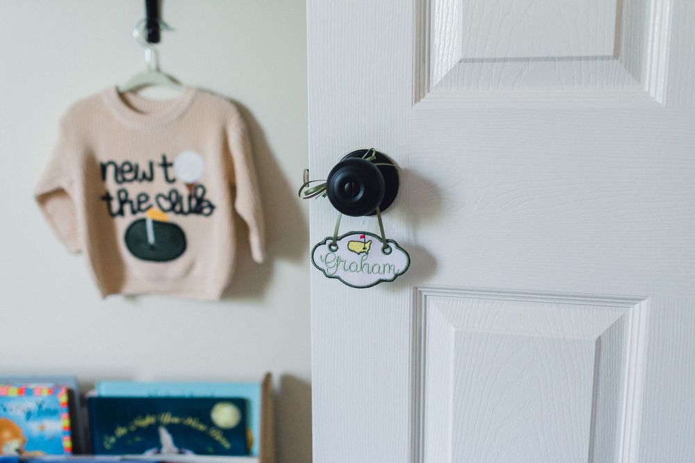 Baby nursery door with a personalized name tag and small sweater hanging nearby.