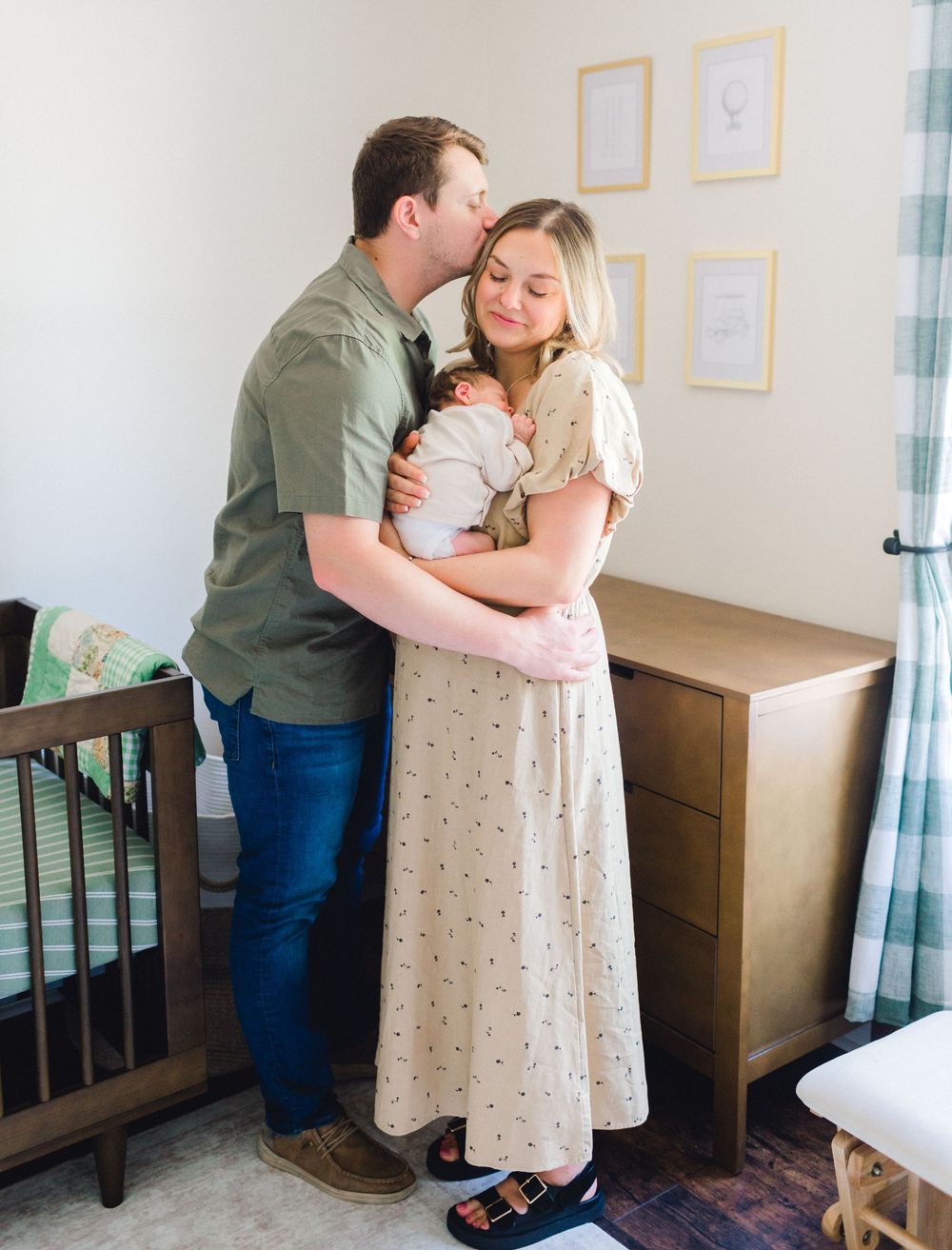 Happy couple shares a tender moment holding their newborn in a serene nursery.