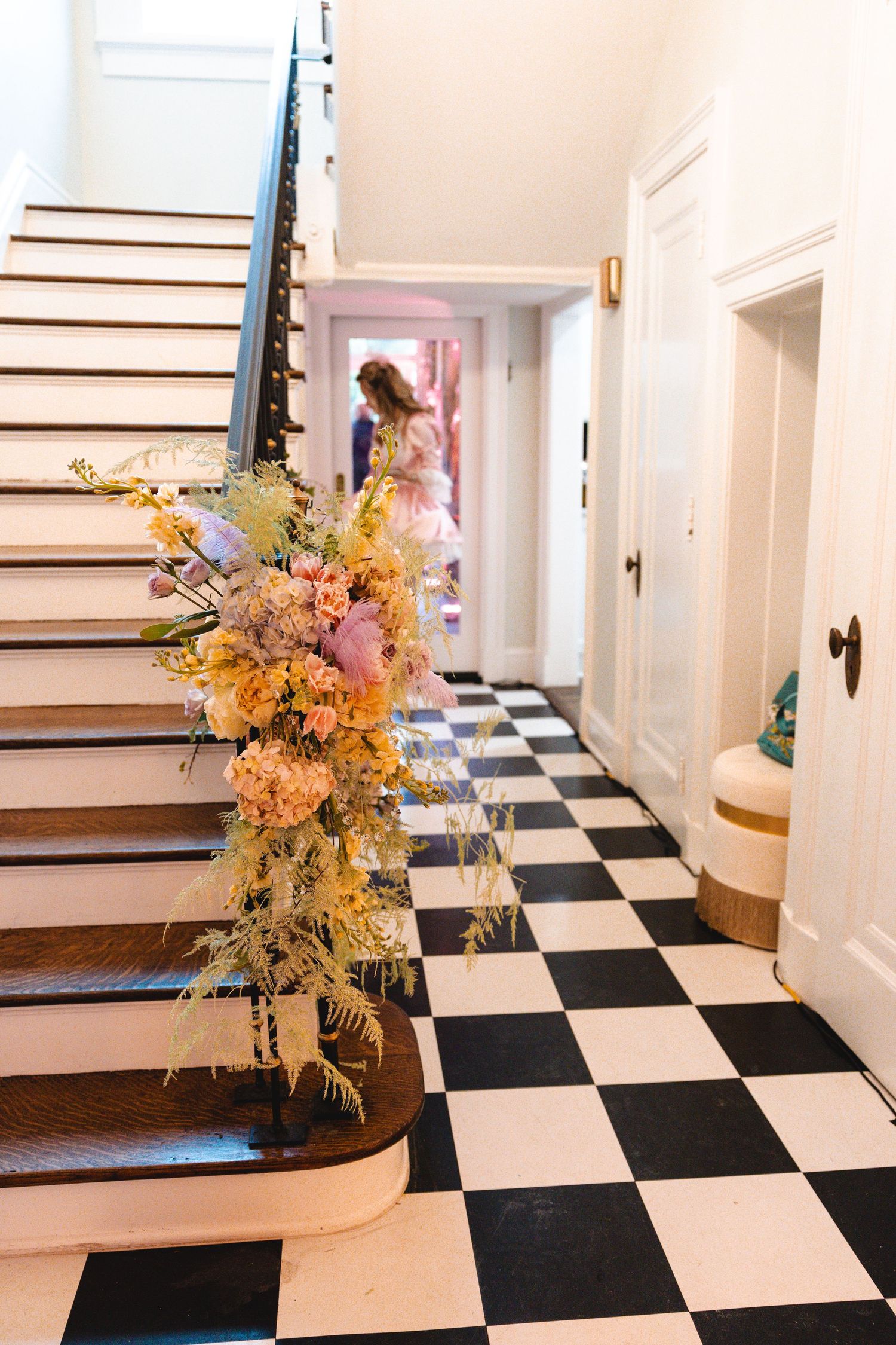 Elegant foyer with black and white checkered floors, wooden staircase adorned with colorful floral arrangement.