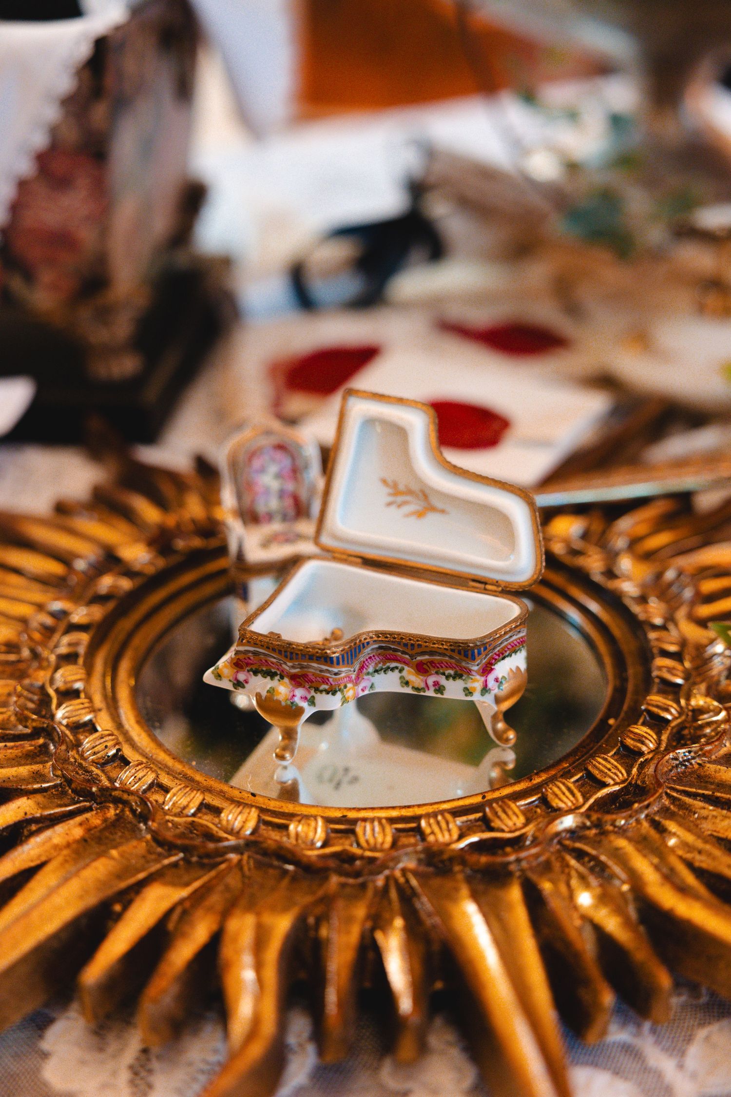 Ornate porcelain grand piano trinket box on a golden sunburst mirror frame at an antique market.