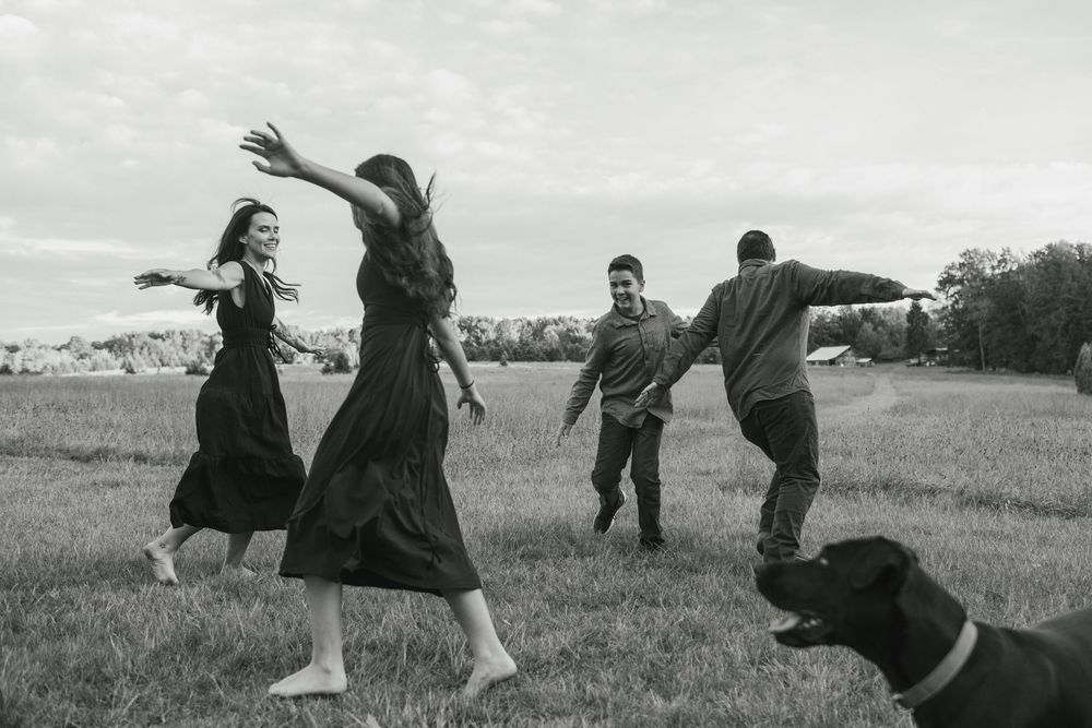 A group of people in dark clothing dance and leap across a grassy field in a series of black and white photographs.
