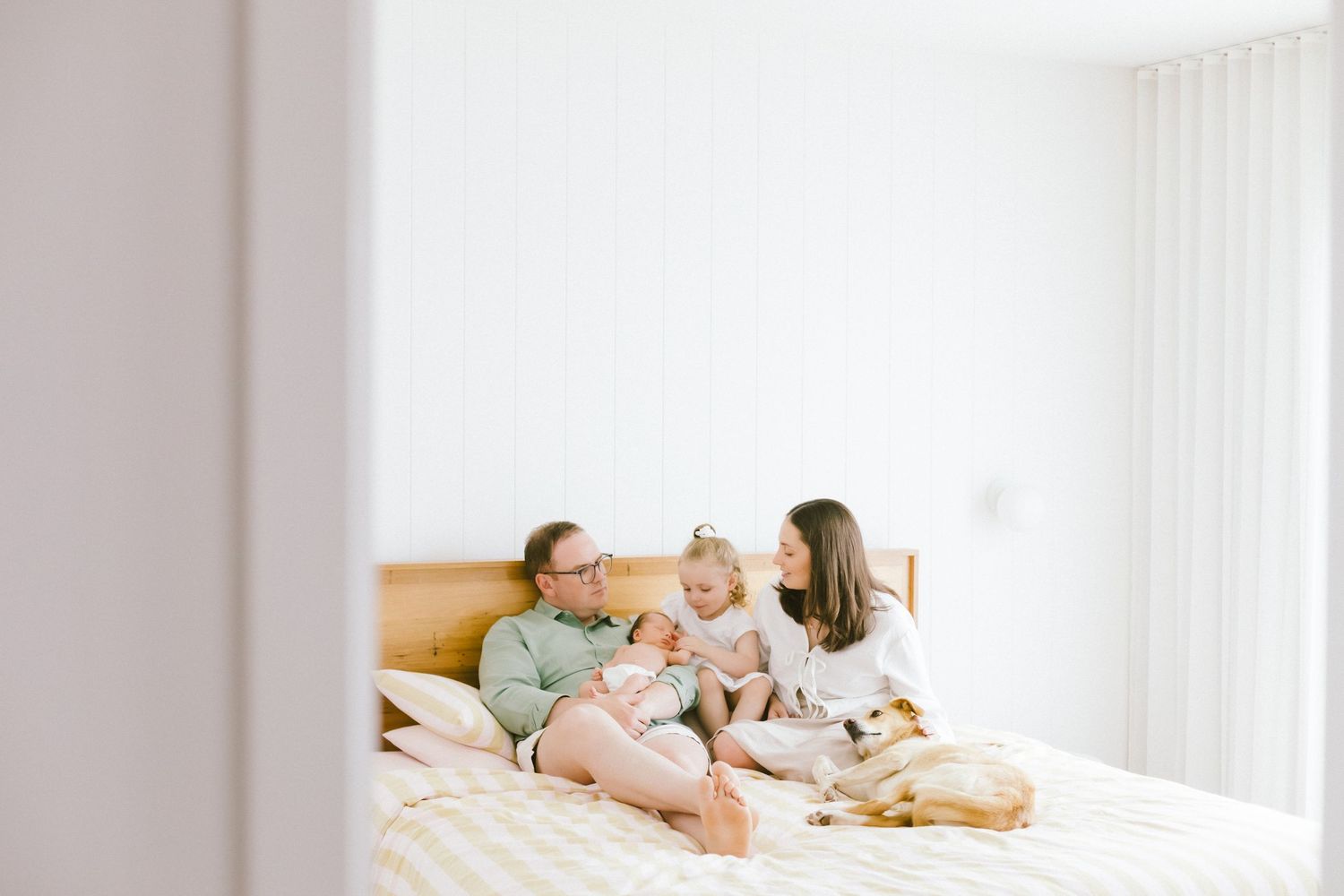 Family with baby and dog relaxing together on a bright white bedroom bed in a modern minimalist home.
