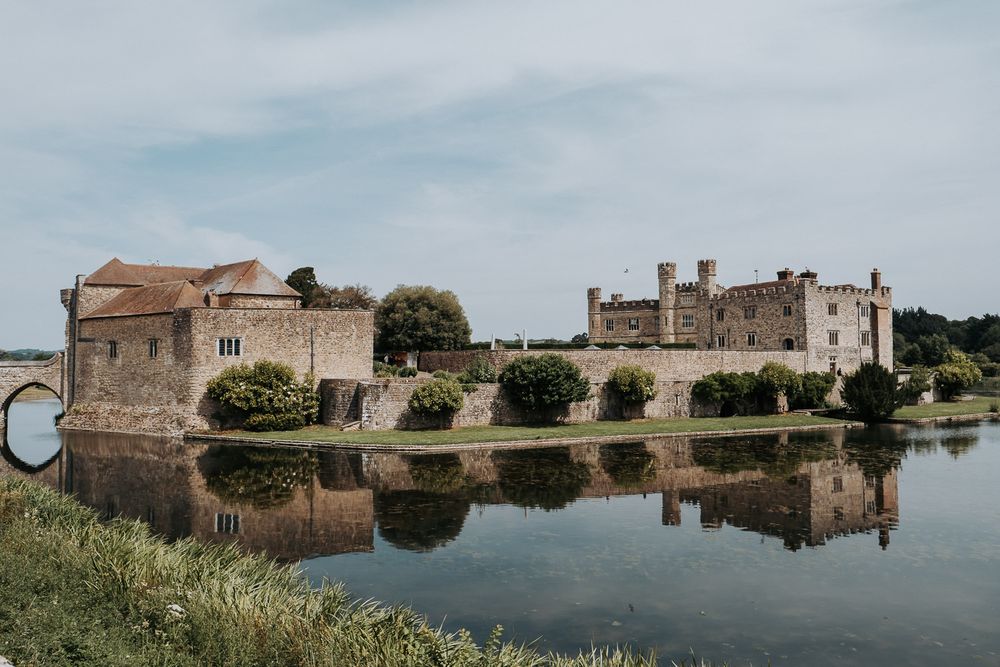 Leeds Castle reflected in its surrounding moat on a cloudy day, showcasing medieval stone architecture in Kent, England.