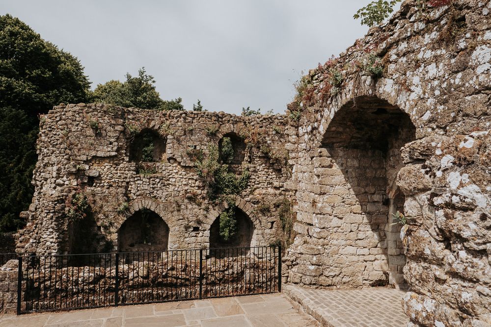 Ancient stone castle ruins with arched windows and doorways, covered in moss and ivy, under an overcast sky.