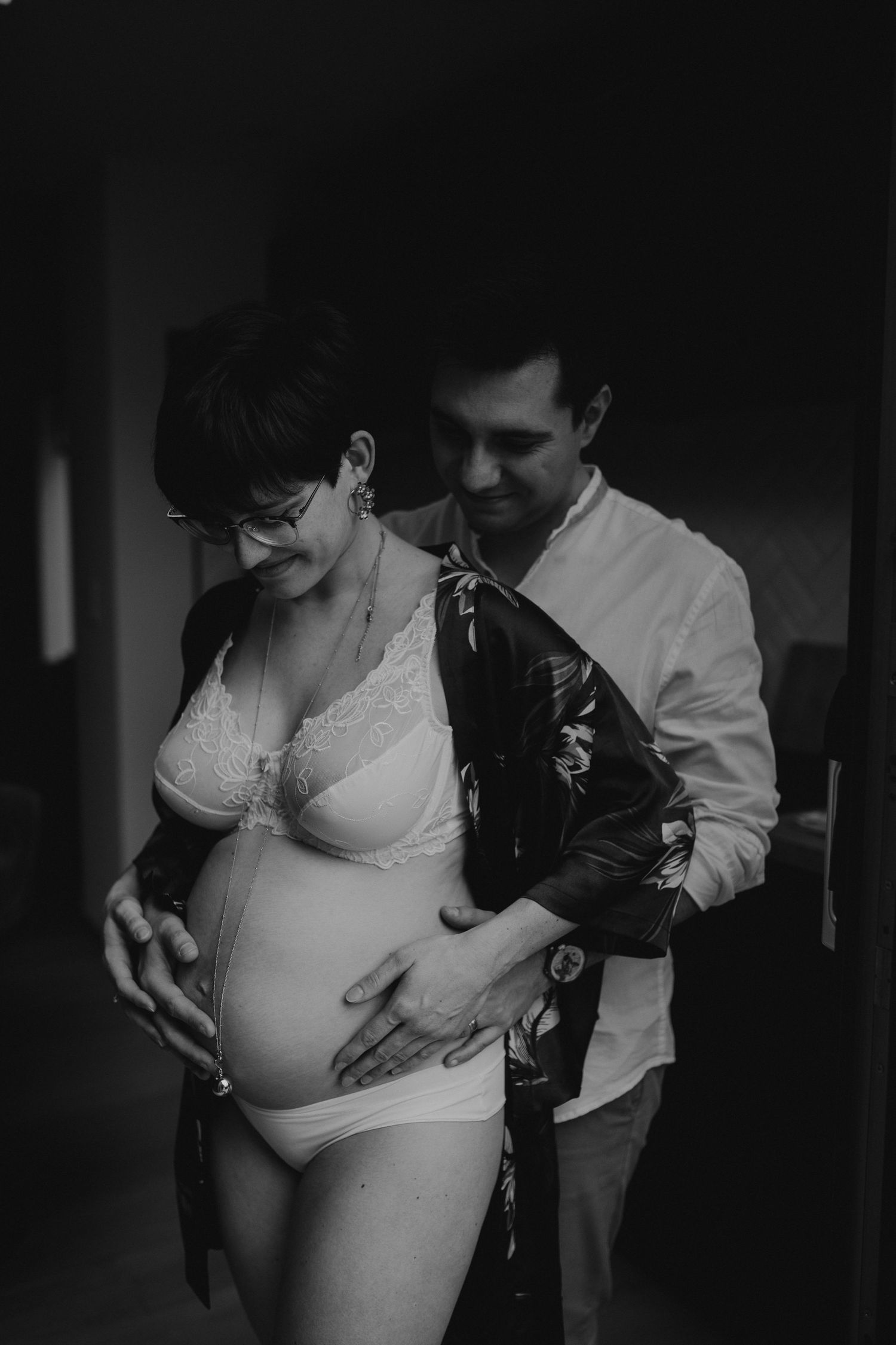 Black and white photo of couple embracing, man holding pregnant womans belly tenderly.