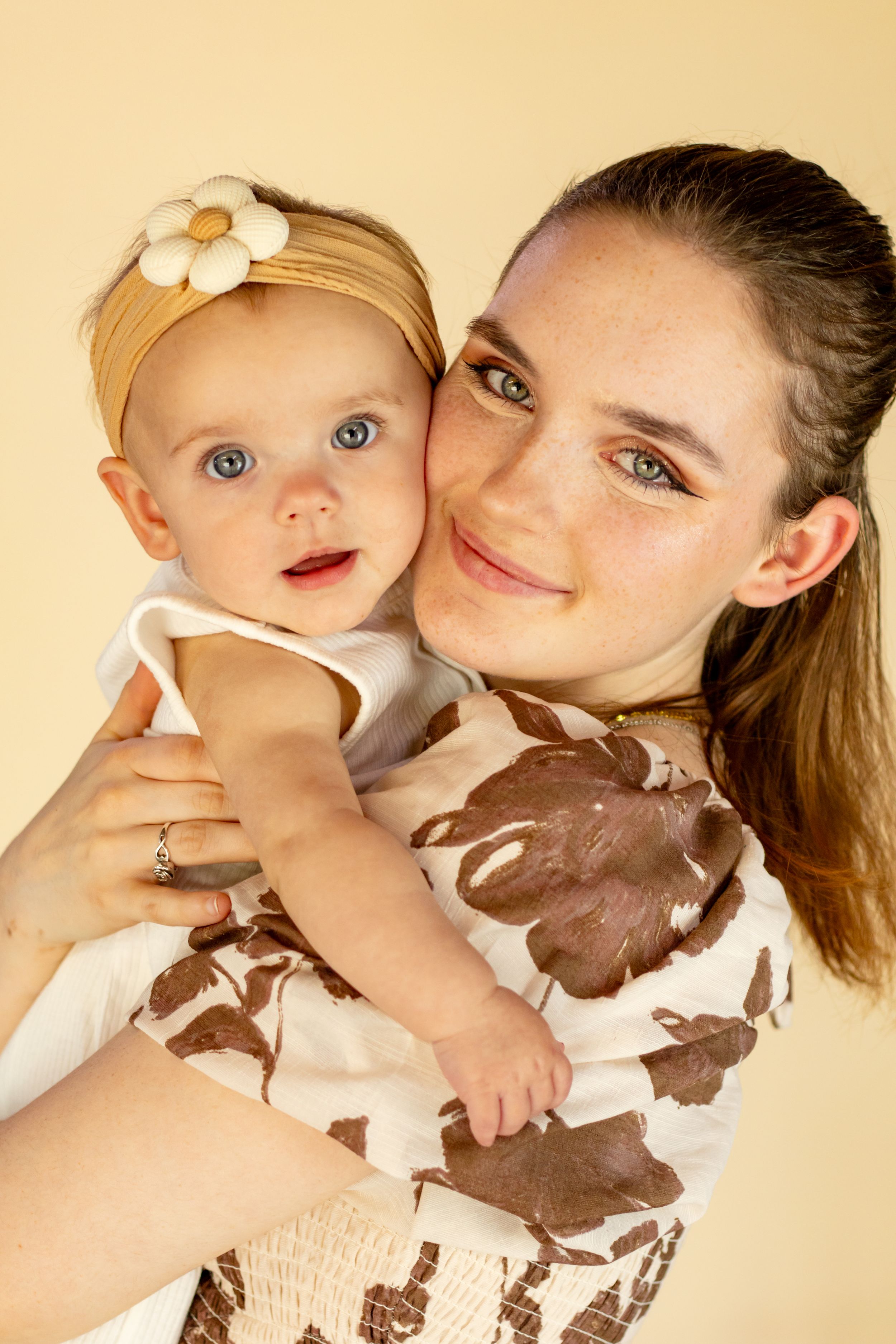 Close-up portrait of young mother with freckles holding blue-eyed baby girl wearing daisy headband taken by pierce county photographer