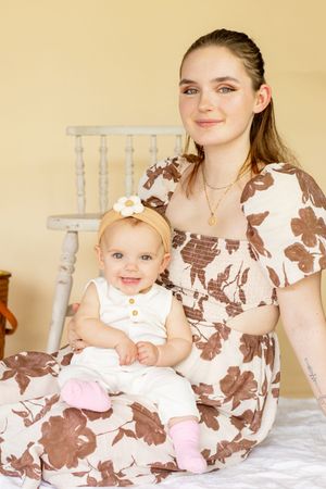 Young mother in floral dress sitting with smiling baby girl wearing daisy headband and pink socks taken by roy wa photographer in studio
