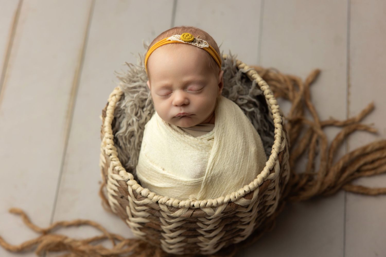 Newborn baby resting chin on hands inside a teal bucket with soft blanket, studio photography.