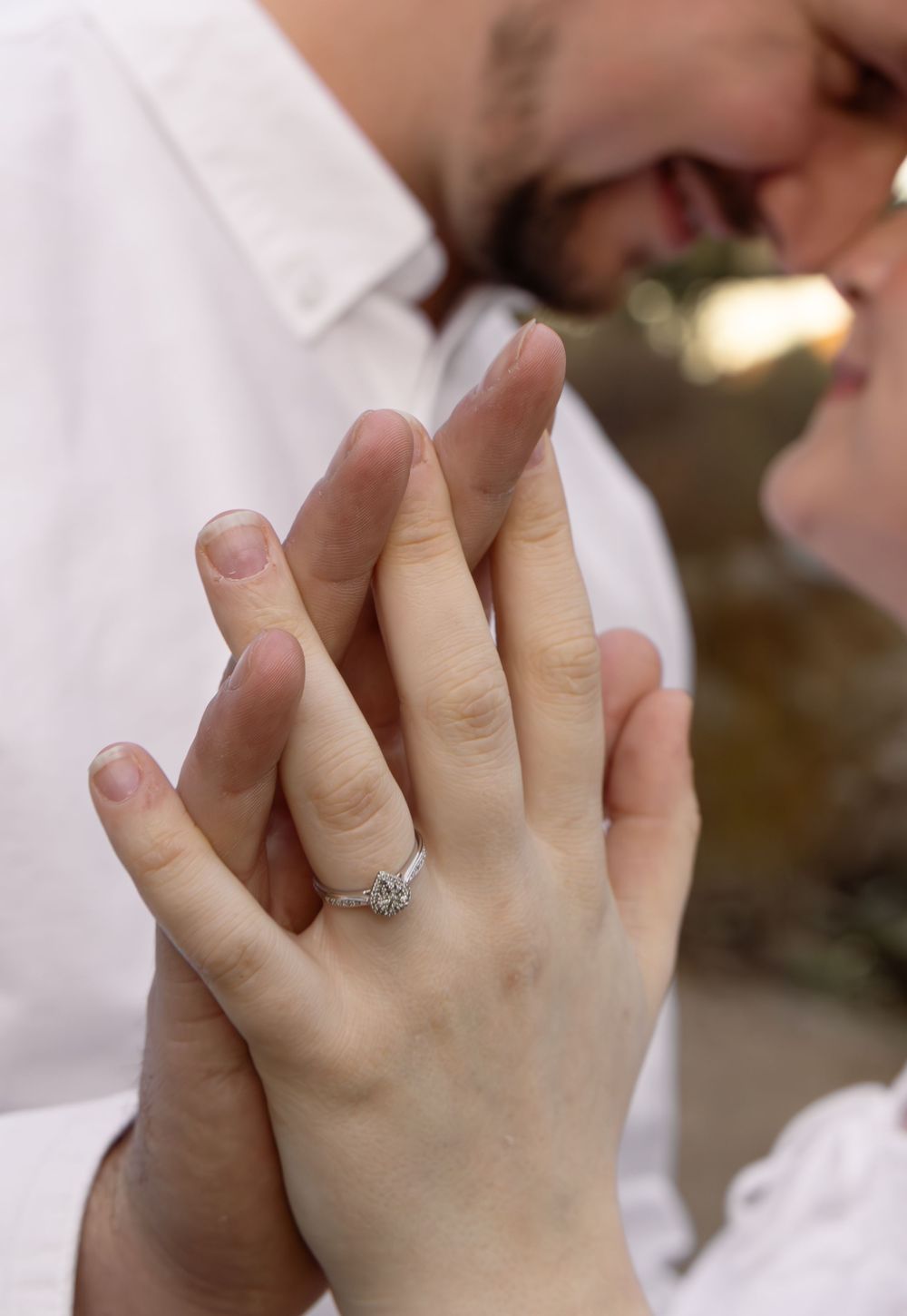 Close-up of an engaged couple holding hands, showcasing a diamond engagement ring, while sharing a romantic moment.