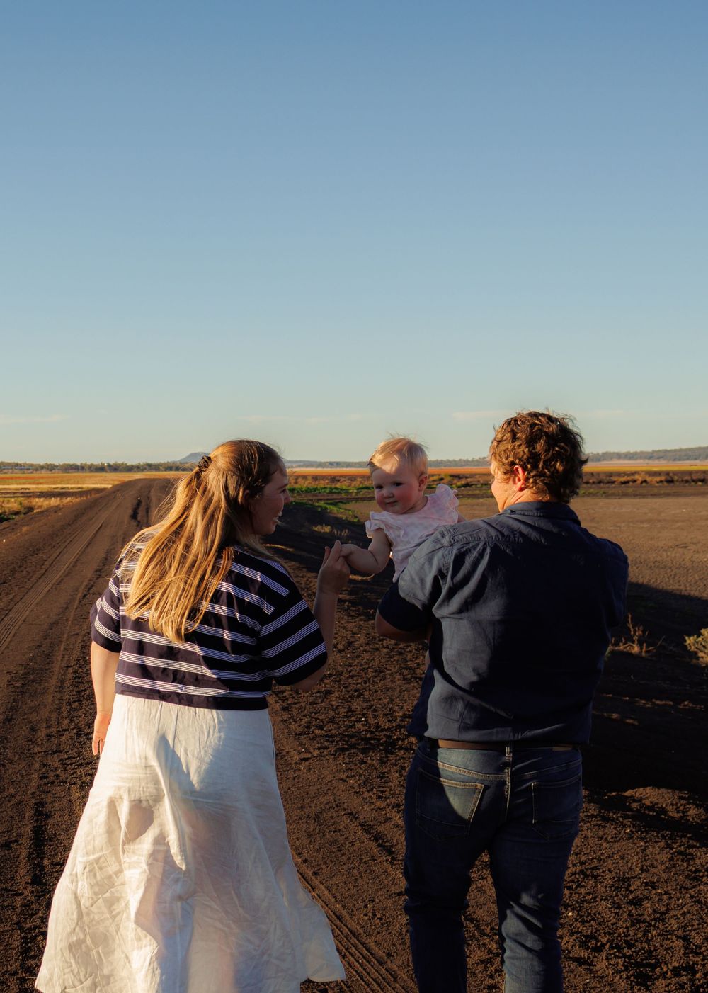 Family of three sharing a tender moment on a rural dirt road at sunset.