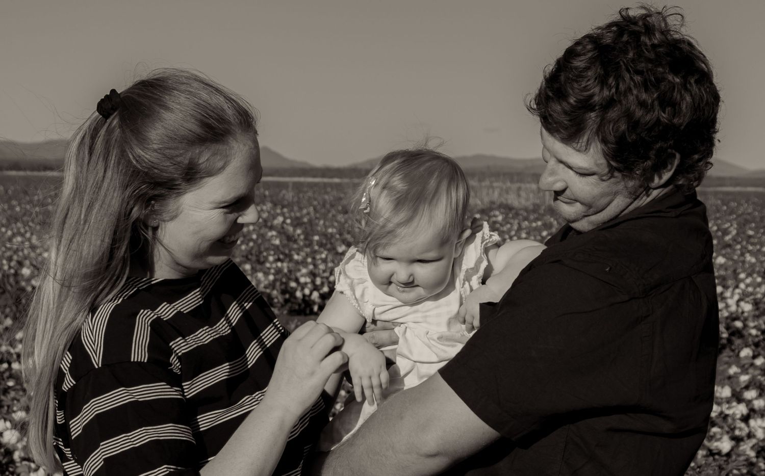 Parents holding baby in black and white photo in cotton field.