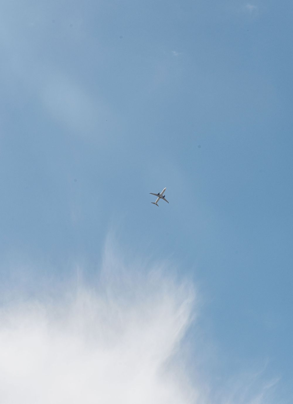 A commercial airplane flying high in a blue sky with wispy white clouds below.
