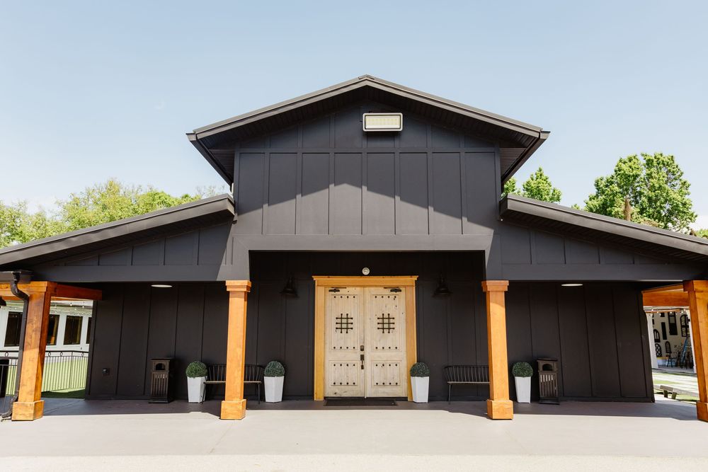 Black barn-style wedding venue exterior with wooden doors and orange columns under a clear blue sky.