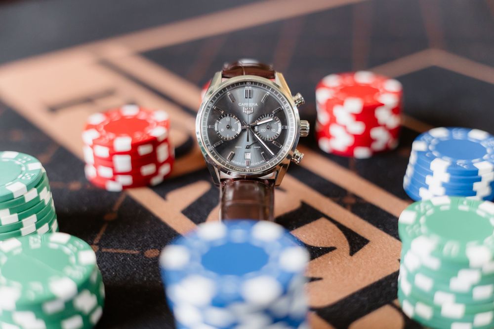 Luxury chronograph watch with brown leather strap displayed on casino table surrounded by colorful poker chips.