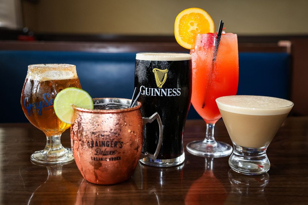 Five colorful bar drinks including Guinness, Moscow mule, cocktails, and a tropical punch on a wooden table.