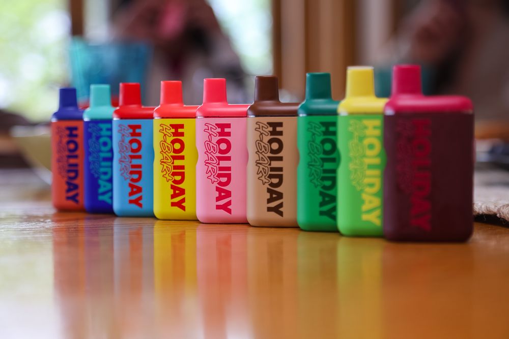 Colorful Holiday branded vape devices lined up in a row on a table, displaying a rainbow of colors.