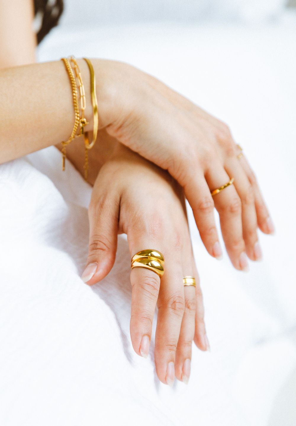 Woman's hands adorned with gold rings and bangles resting on white fabric.