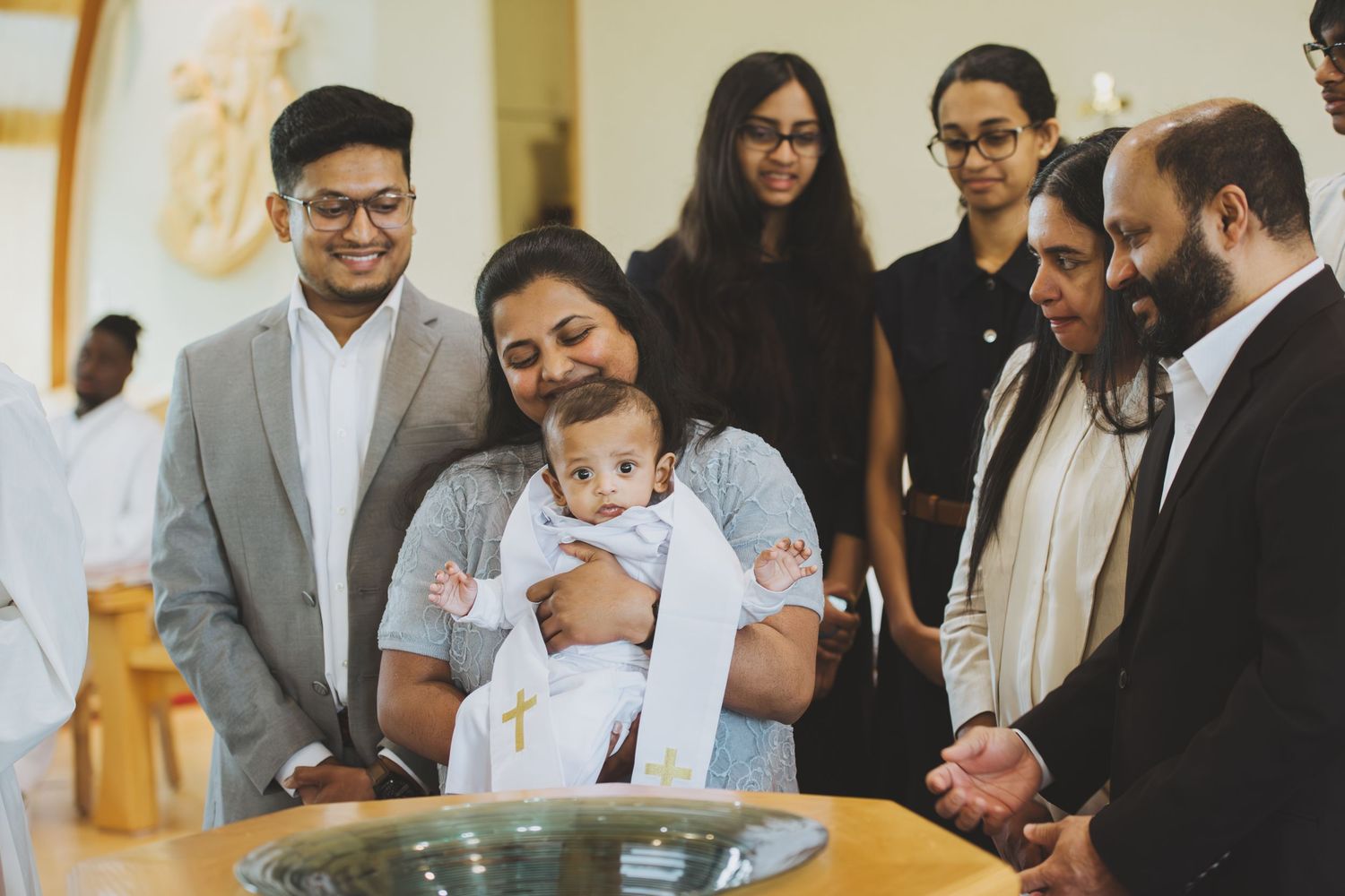 Family gathered around a baptismal font during a baby christening ceremony in a church.