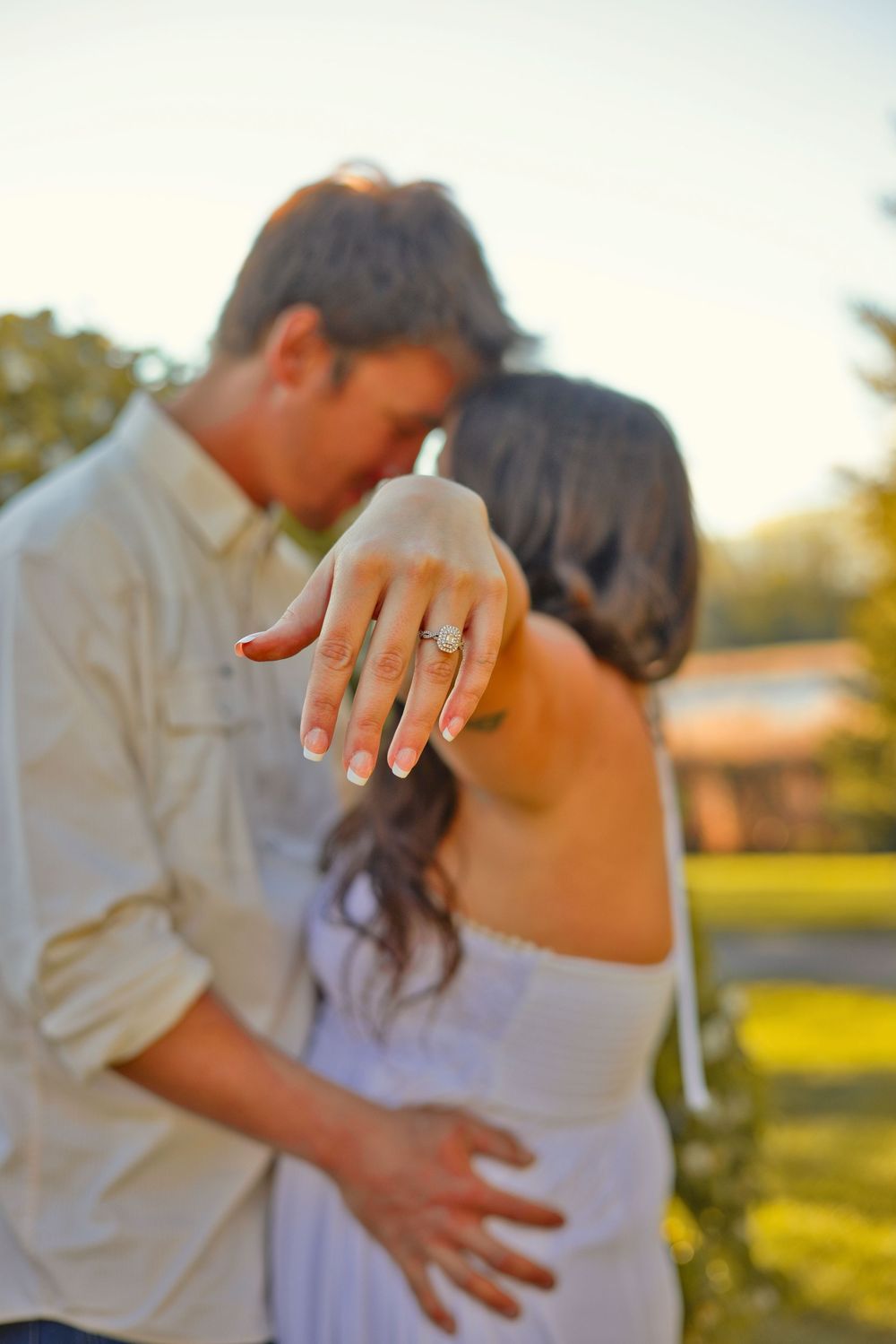 Couple embracing outdoors at sunset, woman showing off diamond engagement ring on her finger.