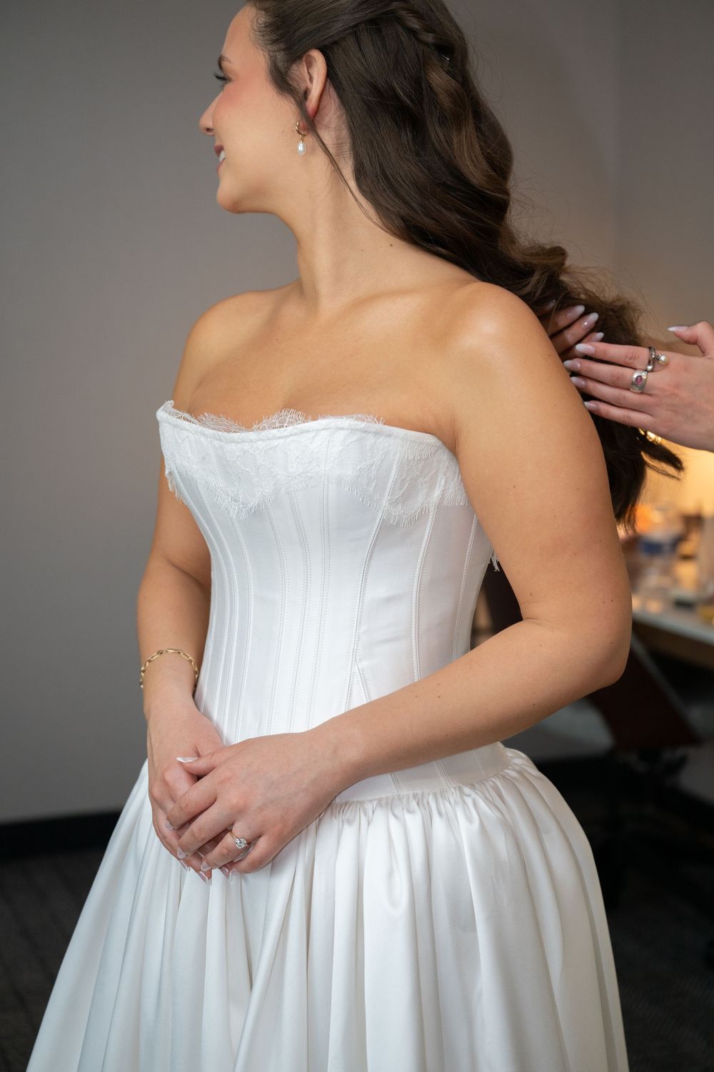 Bride in a strapless white satin corset wedding gown being helped with her hair before the ceremony.