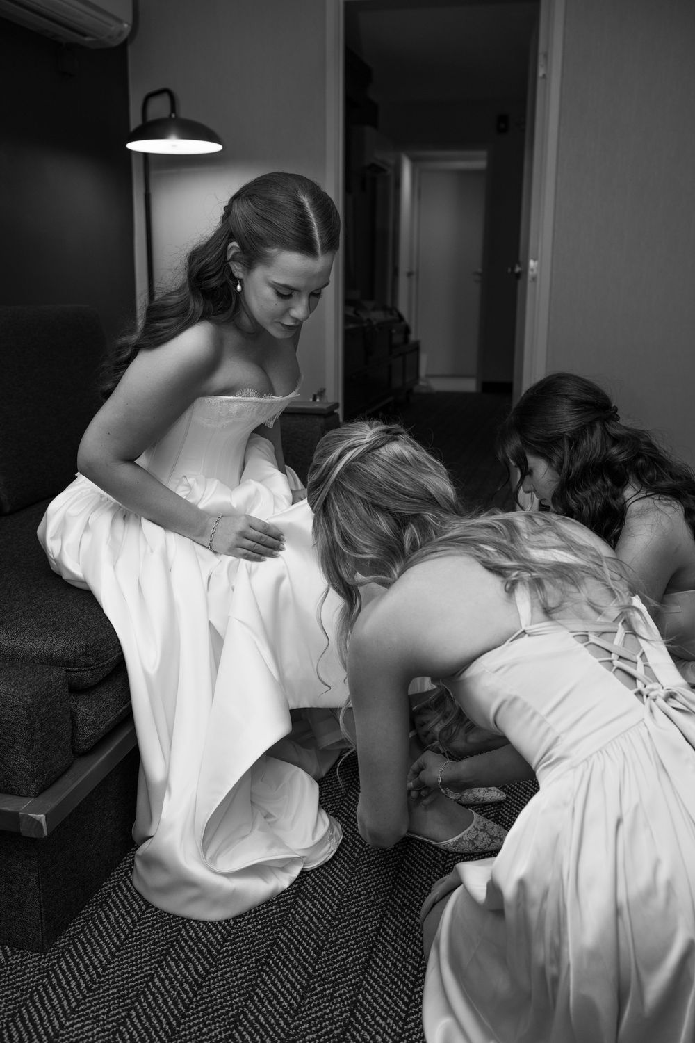 Bridesmaids helping bride with shoes in black and white wedding preparation photo.