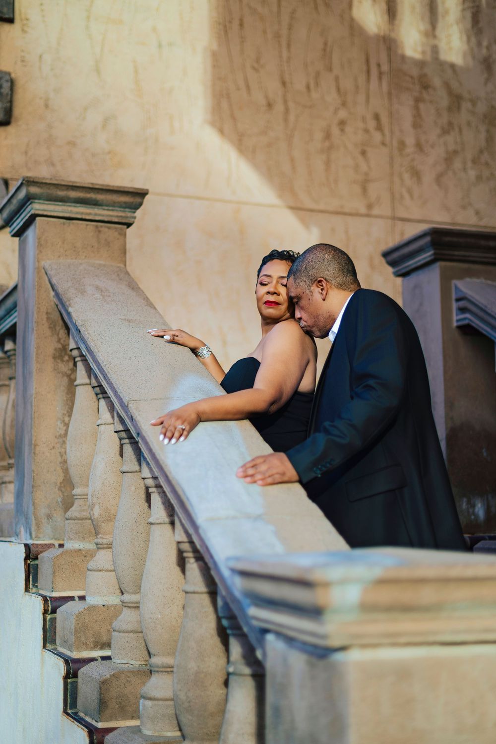 Elegant couple in formal attire sharing a romantic moment on ornate stone staircase with decorative balustrade.