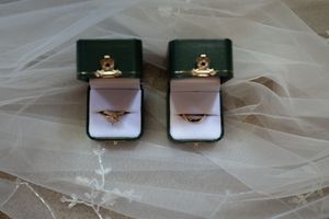 Two gold wedding rings in green velvet boxes displayed on white wedding veil.