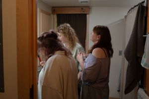 Three women gathered in a hallway during wedding preparations in candid indoor photo.