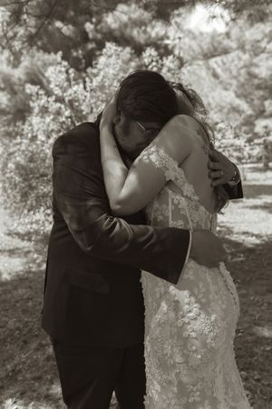 Sepia-toned romantic photo of bride and groom sharing an intimate embrace among trees at their outdoor wedding.