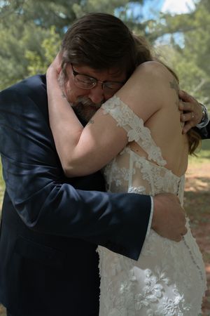 Emotional father embracing his bride daughter in a heartfelt hug during an outdoor wedding celebration.