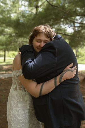 Bride and groom sharing tender embrace in pine forest during wedding first look.