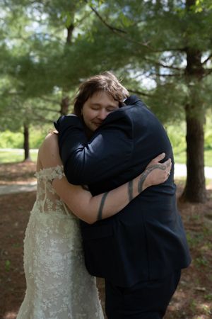 Bride and groom sharing emotional embrace during first look surrounded by pine trees outdoors.