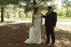 Bride in lace wedding gown with groom in wooded outdoor setting.