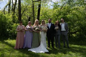 Wedding party group portrait with bride, groom, and bridesmaids in mixed pink and green gowns outdoors.