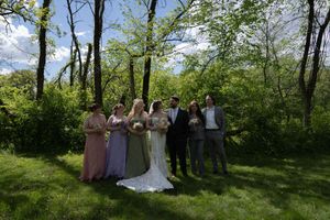Wedding party group portrait with bride groom bridesmaids and groomsmen standing in lush green wooded area.