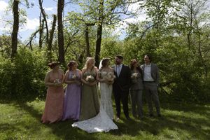 Wedding party poses outdoors in colorful dresses and suits surrounded by lush green trees.