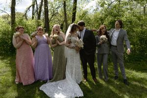 Wedding party celebrating as bride and groom kiss flanked by bridesmaids in pastel gowns and groomsmen outdoors.